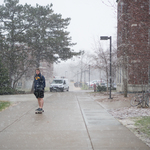 A student skateboards through an early April snow shower.
