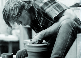 A student working with clay on a potter's wheel